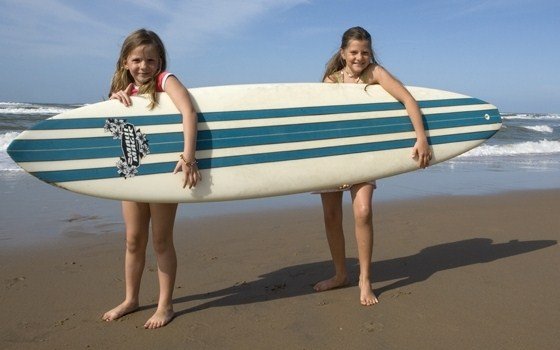 Girls on beach posing with surfboard