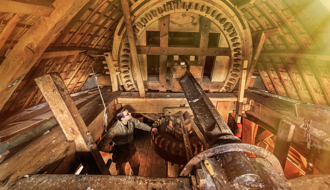 Inside view of a traditional windmill's wooden gear mechanism, with a person examining the structure.