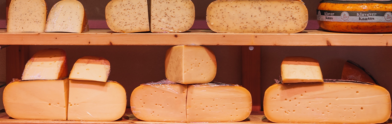 Assorted cheese wheels on shelves, with hues from light yellow to orange.