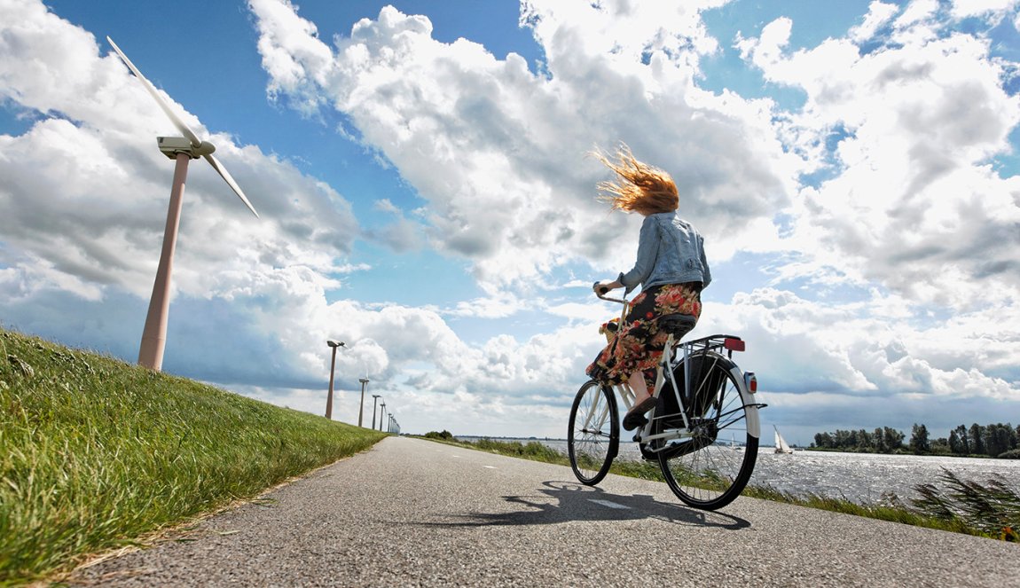 Young woman cycles on a windy road in the Netherlands, wind turbines in the background