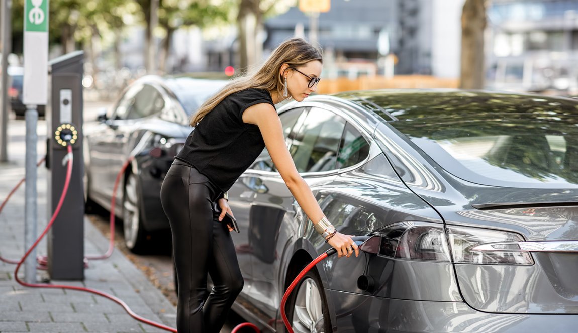 Young woman putting connector into the electric car on the street in Rotterdam