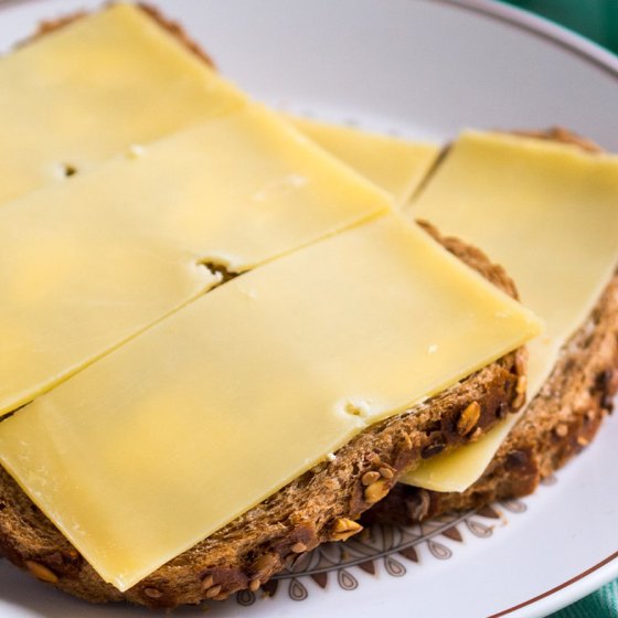 Slices of aged cheese on multigrain bread on a plate with a green checkered napkin.