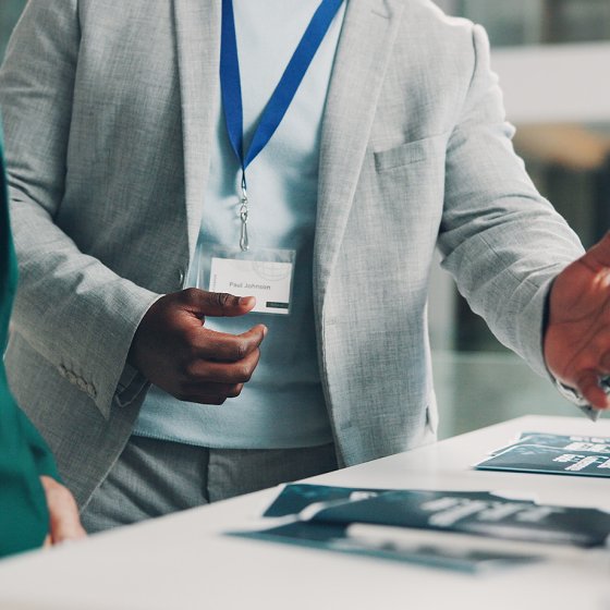 A business visitor talking to a staff member at an information desk at a trade show or conference.