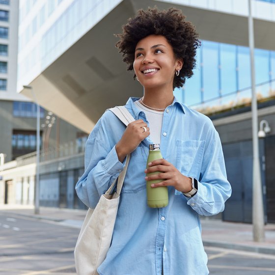 Happy curly haired woman carried fabric bag holds fresh water in bottle