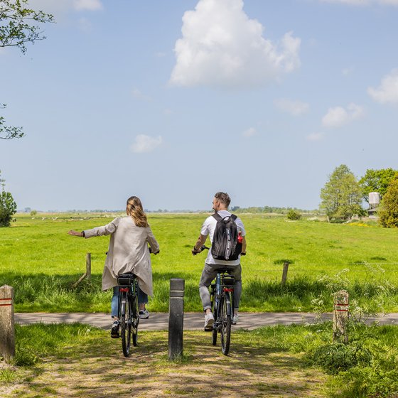 Couple cycling through rural area and holding out hand 