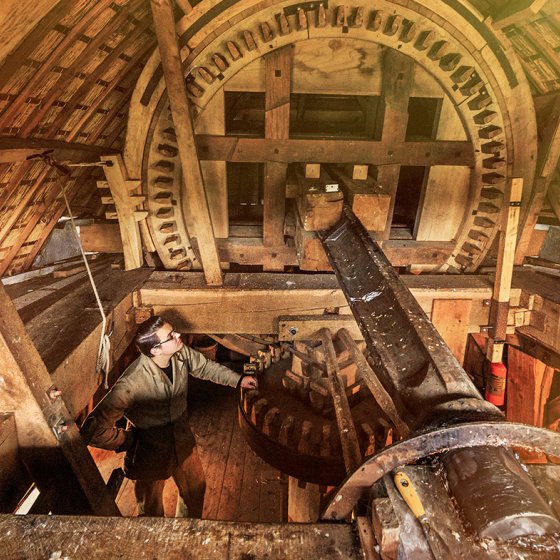 Inside view of a traditional windmill's wooden gear mechanism, with a person examining the structure.