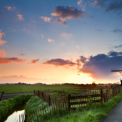 Colored Dutch sky with clouds behind windmill in typical Dutch landscape