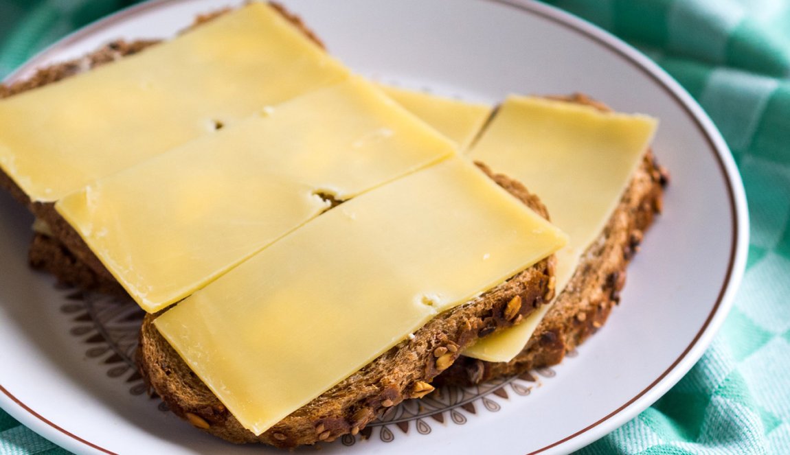 Slices of aged cheese on multigrain bread on a plate with a green checkered napkin.