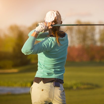 Female golfer swinging golf club on fairway during sunset