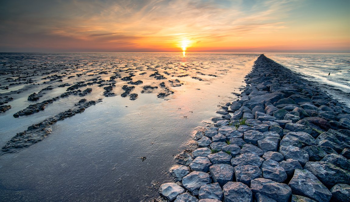 Mud flat of the 'waddenzee' during low tide under scenic dramatic sunset sky with clouds