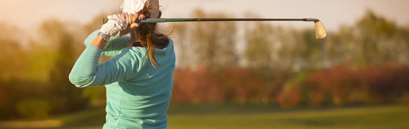 Female golfer swinging golf club on fairway during sunset