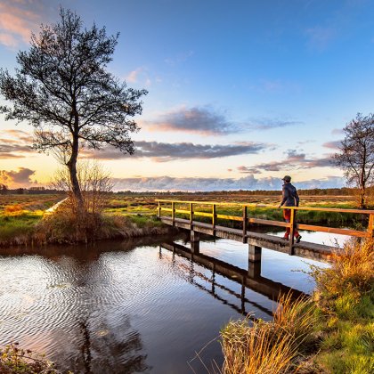 Walker crossing bridge over river in dutch countryside National Park landscape the Drentsche Aa