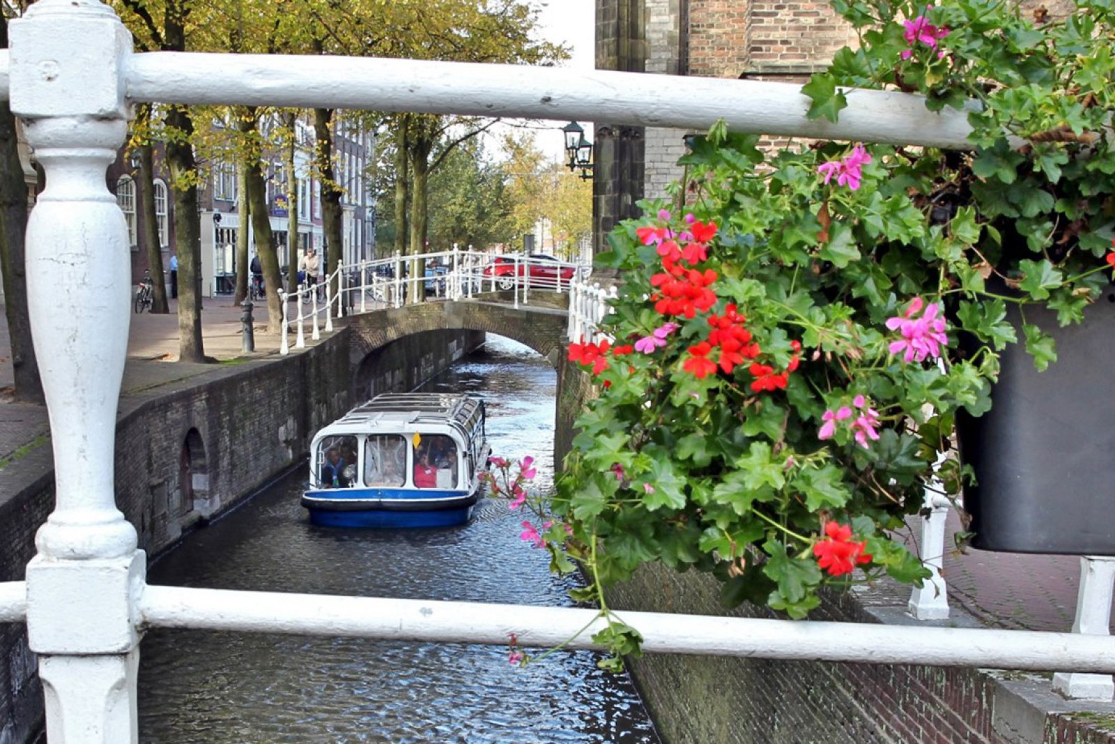 View of boat in canal though the railing of a bridge with a flower pot on the right