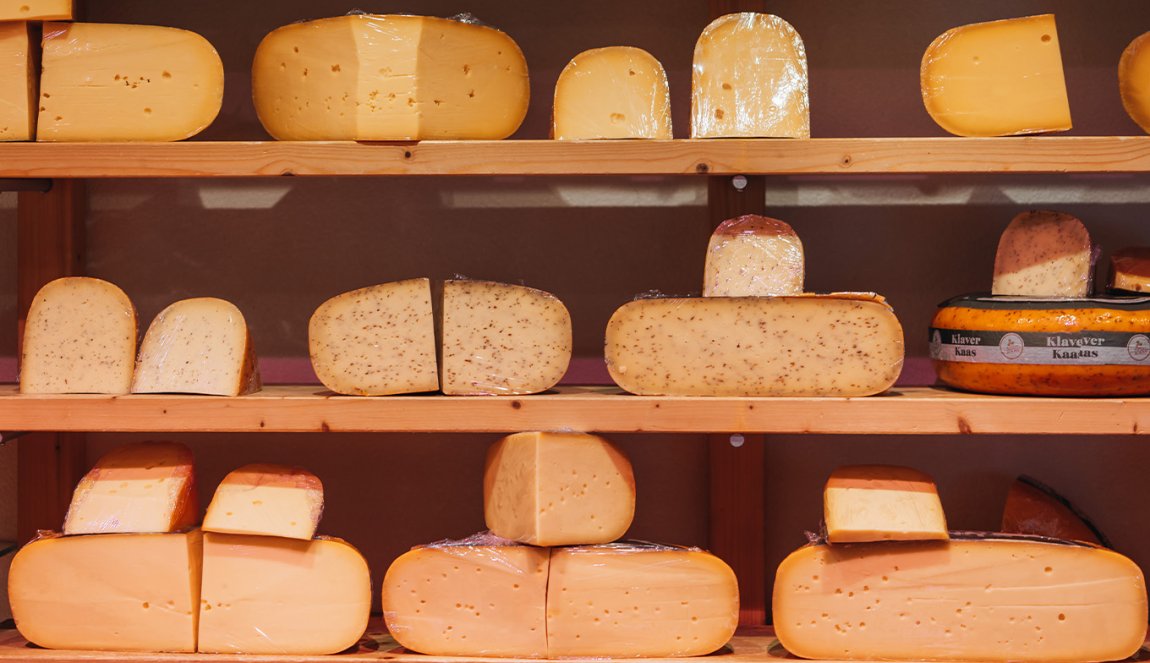 Assorted cheese wheels on shelves, with hues from light yellow to orange.