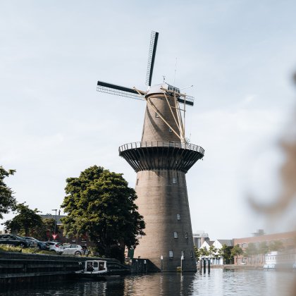 Over-the-shoulder view of a person gazing at 'De Nolet' windmill by a canal