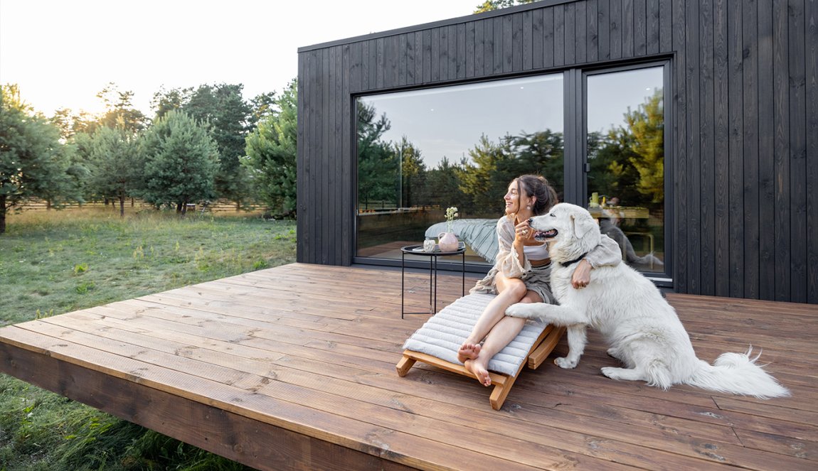Woman sits on sunbed with dog on wooden terrace near the modern vacation house