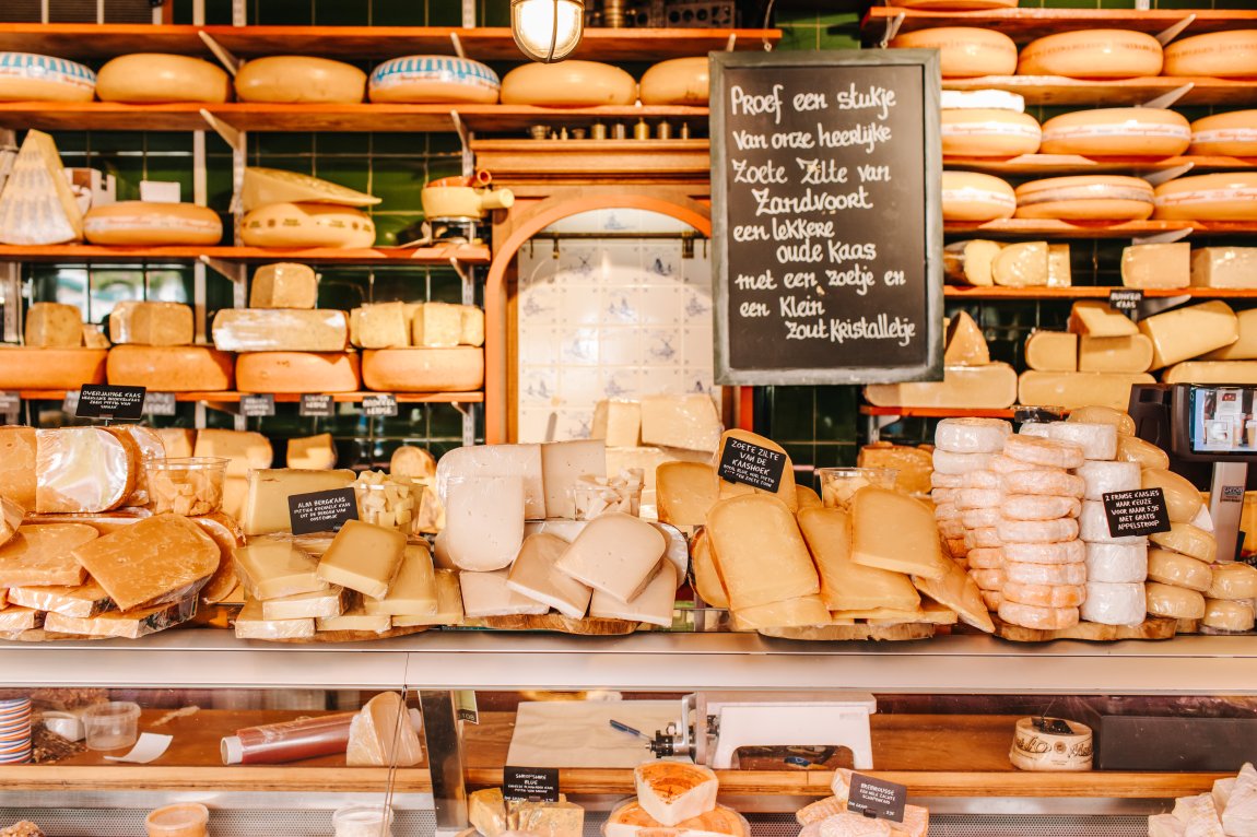 A cozy cheese shop display, with a variety of cheeses and a chalkboard sign inviting customers to taste.