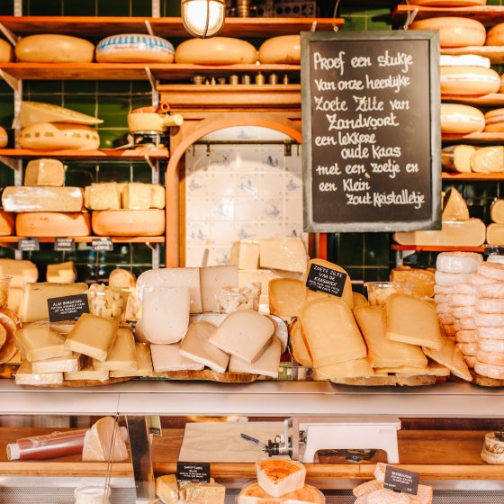 A cozy cheese shop display, with a variety of cheeses and a chalkboard sign inviting customers to taste.