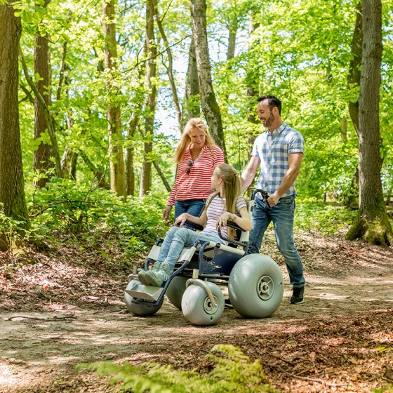 Parents walk through nature reserve De Duivelsberg, Gelderland with daughter in wheelchair.