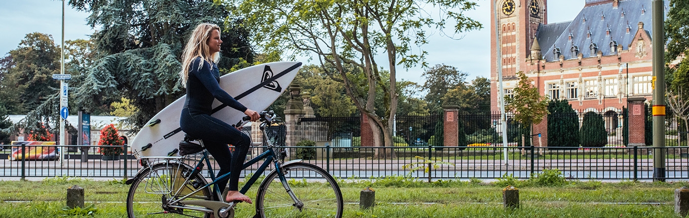 Women with a surfboard riding on a bike