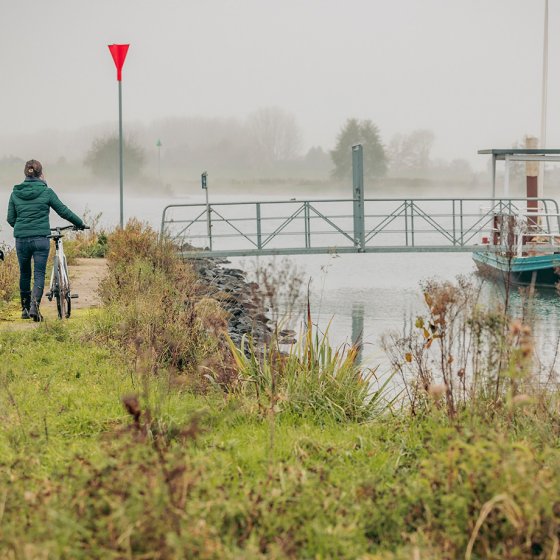 Cyclists walking their bikes along a dike near Schalkwijk in the Utrecht region on a misty autumn day