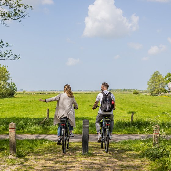 Couple cycling through rural area and holding out hand 