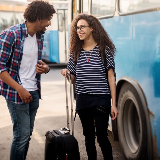 Young happy couple standing and talking in front of the bus with their suitcase