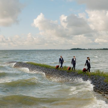 Three business travellers with suitcases walking along a breakwater in Friesland.