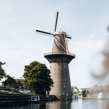 Over-the-shoulder view of a person gazing at 'De Nolet' windmill by a canal
