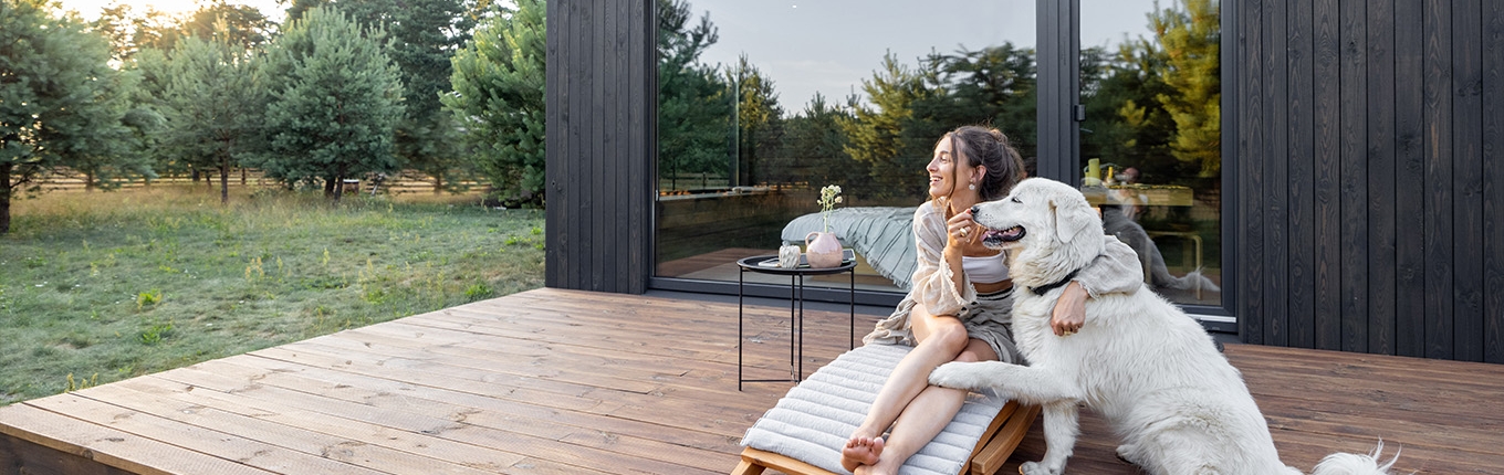 Woman sits on sunbed with dog on wooden terrace near the modern vacation house Woman sits on sunbed with dog on wooden terrace near the modern vacation house