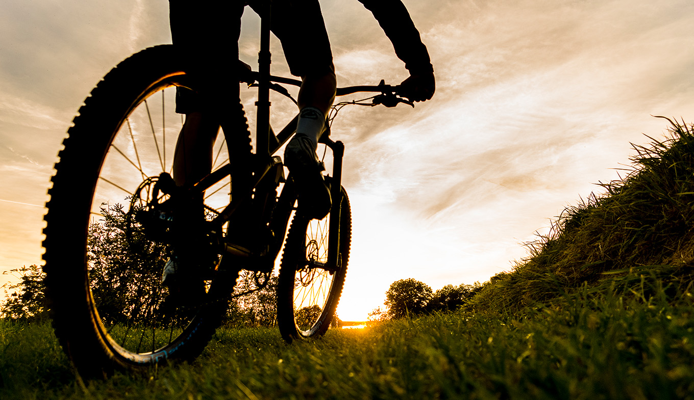 Mountain biker Heuvelland on the road on grass sun in the background