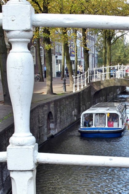 View of boat in canal though the railing of a bridge with a flower pot on the right