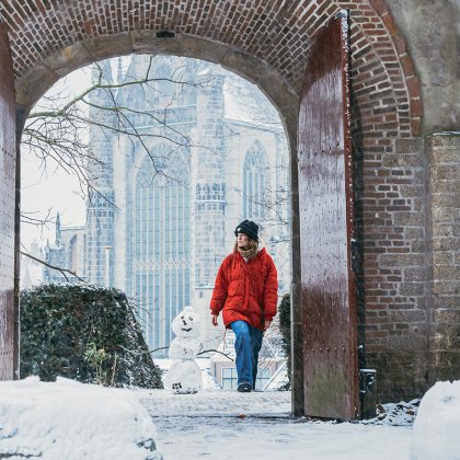 Snow covers De Burcht in Leiden in 2025, as a person wearing a red coat walks by
