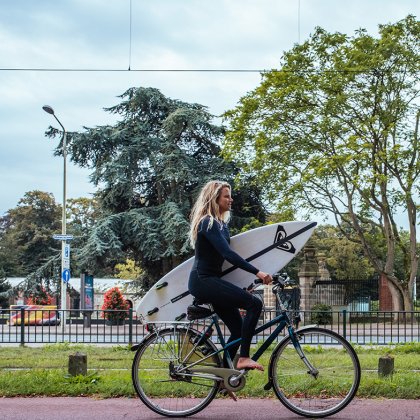 Women with a surfboard riding on a bike The Hague
