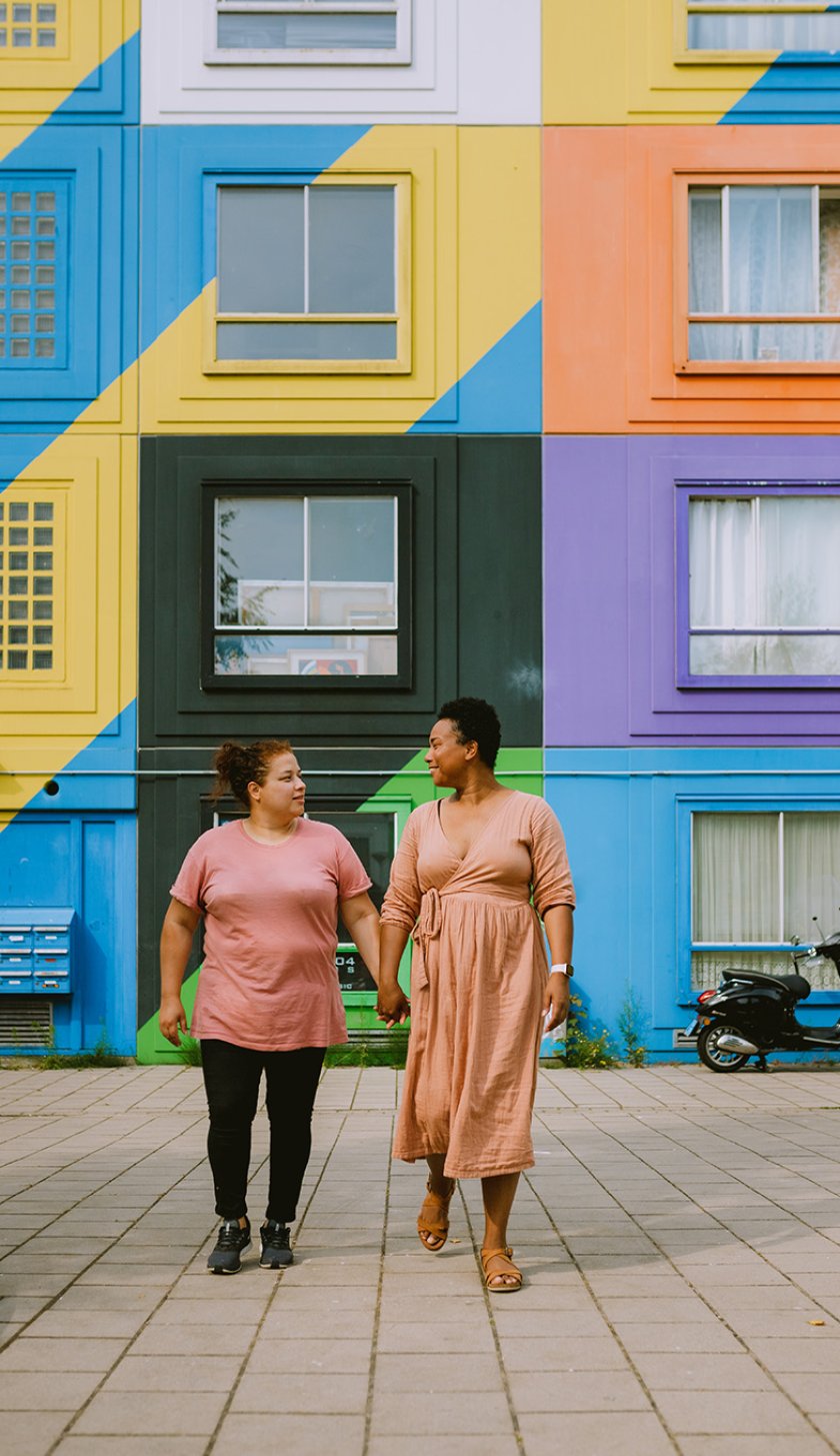 Couple walking hand in hand in front of colorful housing complex in Heesterveld, Amsterdam