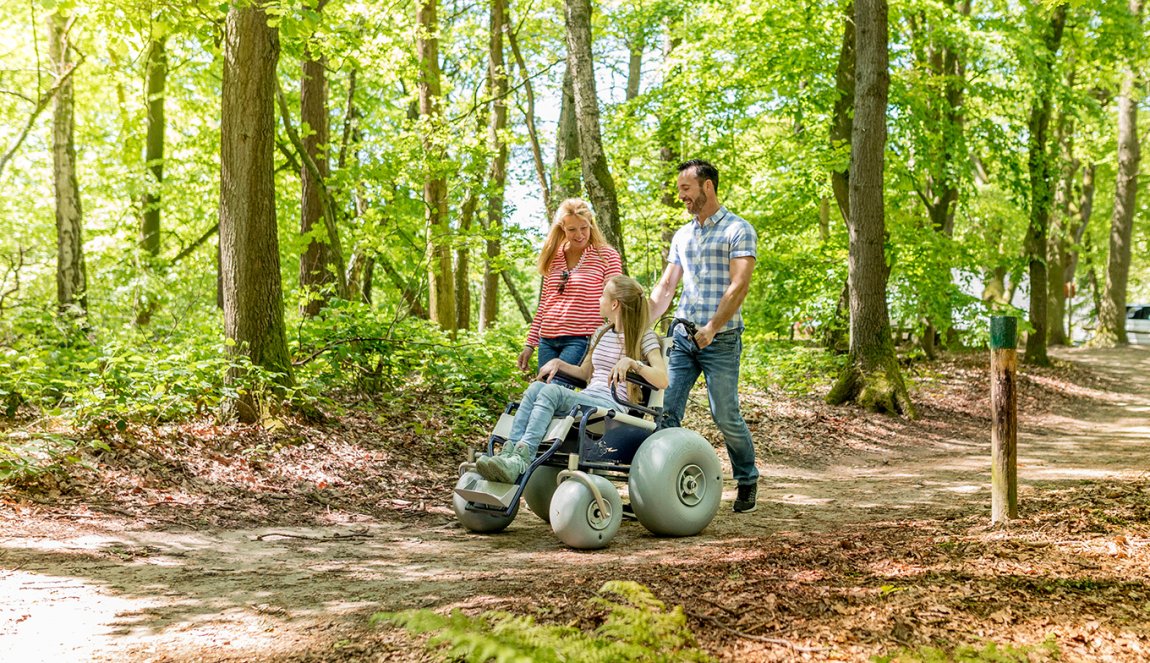 Parents walk through nature reserve De Duivelsberg, Gelderland with daughter in wheelchair.