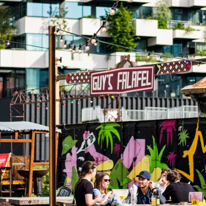 People enjoying food and drinks on a sunny terrace at Ketelhuisplein in Eindhoven's Strijp-S district, a lively destination for outdoor dining and creative city experiences