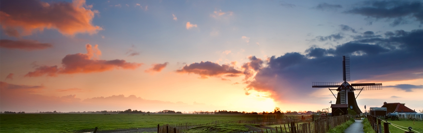 Colored Dutch sky with clouds behind windmill in typical Dutch landscape