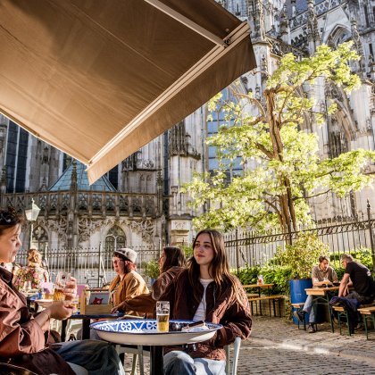 Friends enjoying drinks on a sunny terrace beside St. John's Cathedral in 's-Hertogenbosch, combining local hospitality with a historic city atmosphere