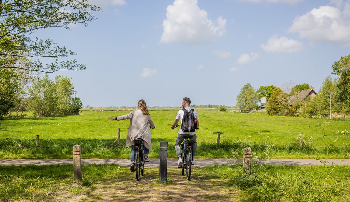 Couple cycling through rural area and holding out hand 