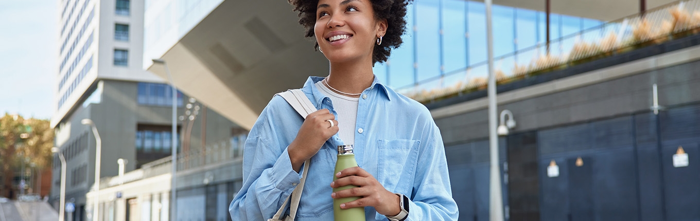 Happy curly haired woman carried fabric bag holds fresh water in bottle