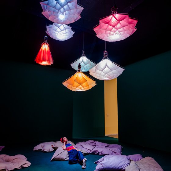 Visitor relaxing beneath illuminated flower-shaped artworks at Flowers Forever in Kunsthal Rotterdam
