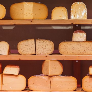 Assorted cheese wheels on shelves, with hues from light yellow to orange.
